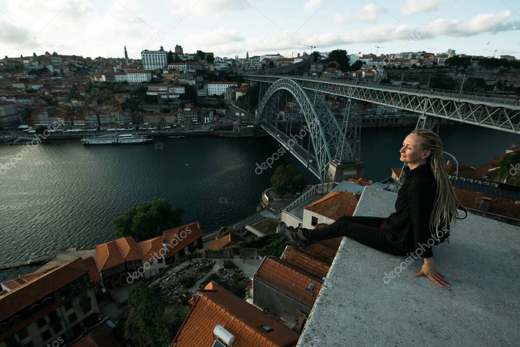 Woman sitting in front of Douro river and Dom luis I bridge in the gloomy weather, Porto, Portugal. 