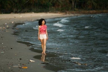 Asyalı kadın kirlenmiş tropikal bir plajda yürüyor.. 