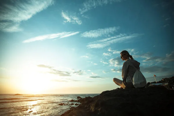 日落时坐在岩石海岸上的年轻女子 — 图库照片