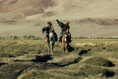 BAYAN-OLGII, MONGOLIA - SEP 28, 2017: Berkutchi (Kazak Kartal Avcısı) Bayan-Olgii aimag dağlarında kollarında altın kartallarla avlanırken.