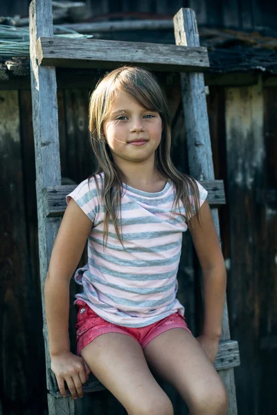 村里一个小女孩坐在木楼梯上的画像 — 图库照片