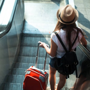 Elinde bavulu olan kız yürüyen merdivenden aşağı iniyor..