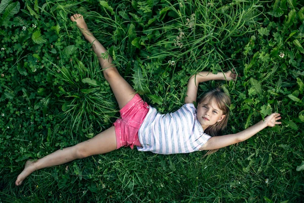 上から見る 少女は緑の芝生の上で腕を伸ばして横になっている — ストック写真