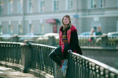 Genç bir kız Saint Petersburg 'daki nehir kenarının korkuluklarında oturuyor..