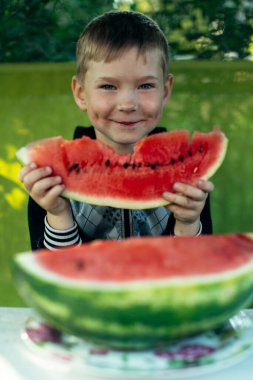 Küçük gülümseyen bir çocuk bahçede karpuz yiyor..
