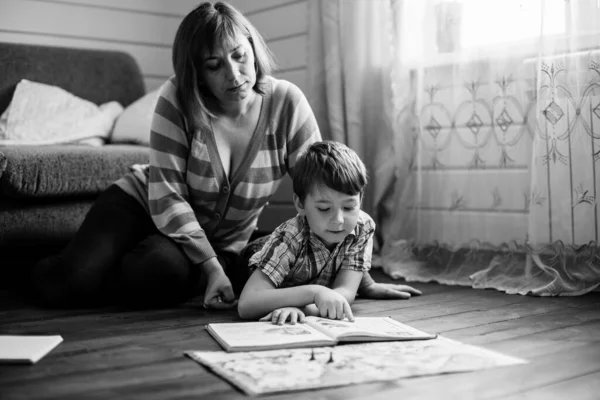 家の床に小さな息子と一緒に本を読んでいる若い女性 白黒写真 — ストック写真