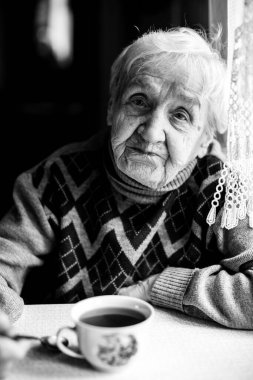 Masada süveterle oturan yaşlı bir kadın portresi. Siyah beyaz fotoğraf.