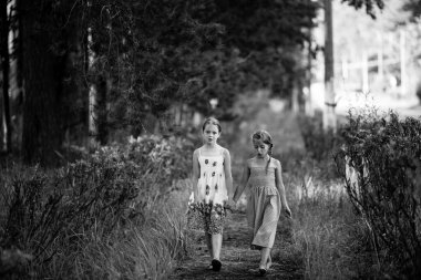 On yaşındaki iki kız arkadaş parkta yürür. Siyah beyaz fotoğraf.