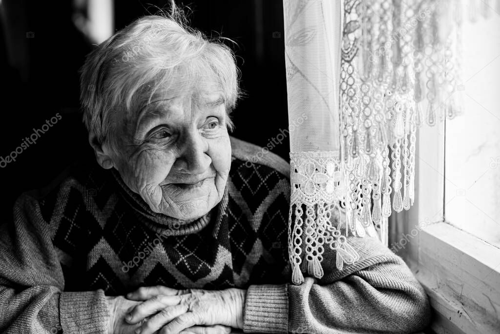 Portrait of happy old woman sitting at the table. Black and white photography.