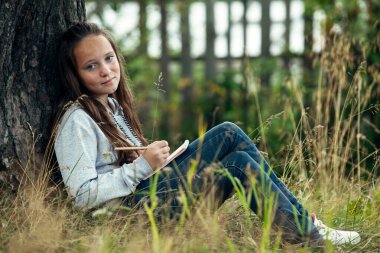 Parkta otururken not defterine yazan genç kız..