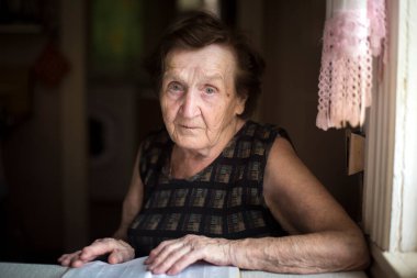 Masada elinde dergiyle oturan buruşuk bir kadının portresi..