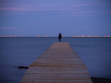 Mar Menor 'da geceleri bir iskeleden rahat bir kişi sakin deniz düşünüyor