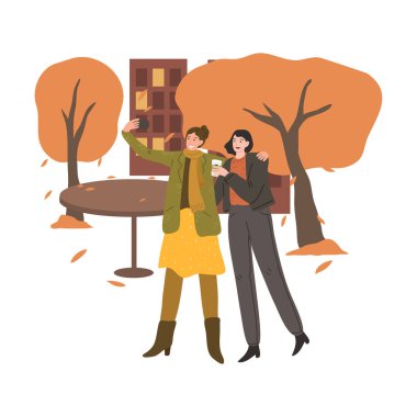 Gülümseyen kızlar, güz şehrinde dışarıda kahve içip selfie çekiyorlar.