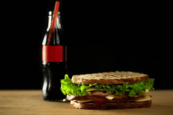 two club sandwiches with sauce and bottle soft drink on wooden board.