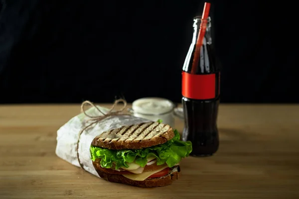 two club sandwiches with sauce and bottle soft drink on wooden board.