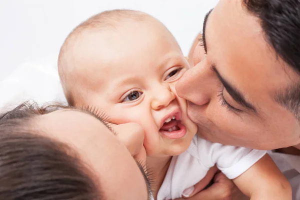 Parents kissing baby in the house.