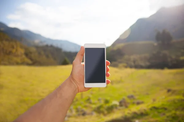 Close up - hand holding smartphone, landscape on background