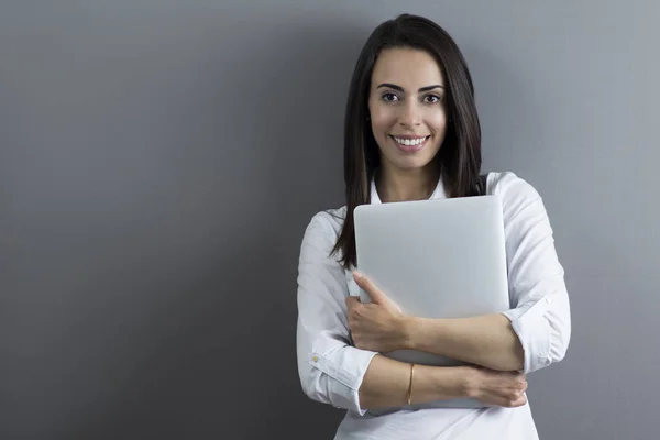 Young business woman holding a laptop on gray background