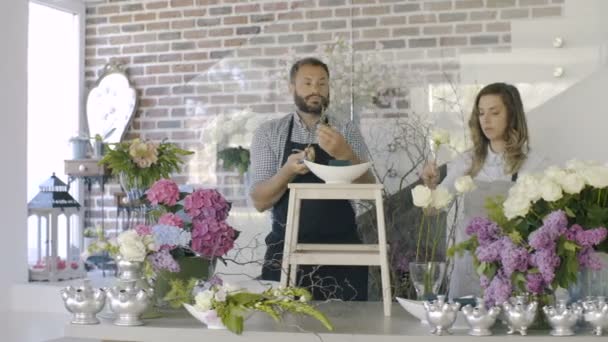Atractiva pareja de trabajos de floristería en floristería sobre fondo de flores . — Vídeo de stock