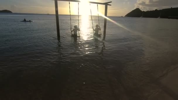 Силуэт двух женщин, качающихся на качелях в воде на закате — стоковое видео