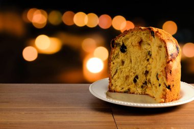 closeup panettone seramik plaka üzerinde ahşap masa, bokeh arka ışıklı, önden görünüm