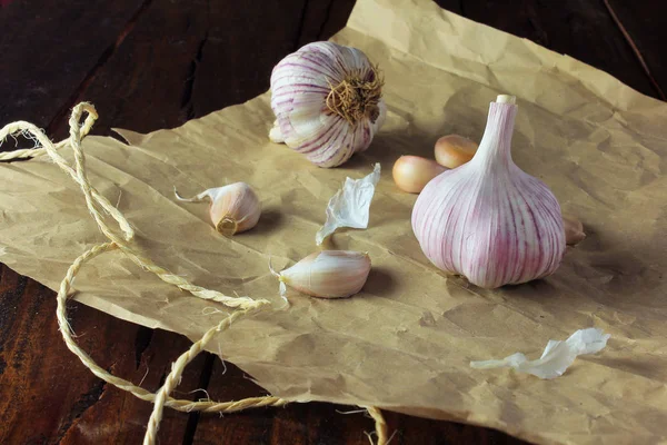 Garlic bulbs on packing paper, on rustic wooden table. Closeup of garlic bulbs.