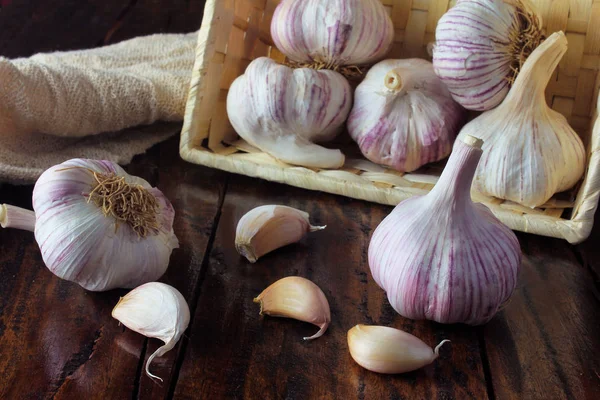 Garlic bulbs inside basket of straw, on rustic wooden table. Closeup of garlic bulbs.