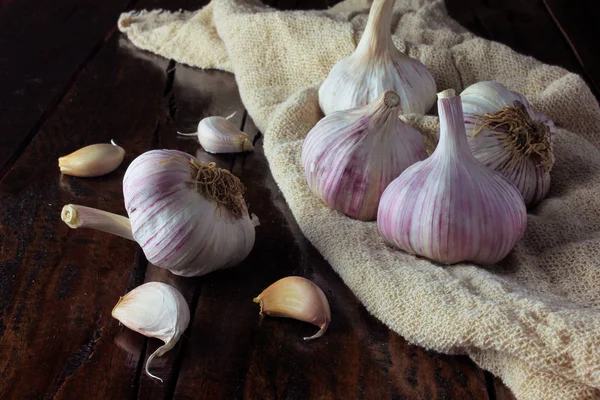 Garlic bulbs on rustic fabric, on rustic wooden table. Closeup of garlic bulbs.