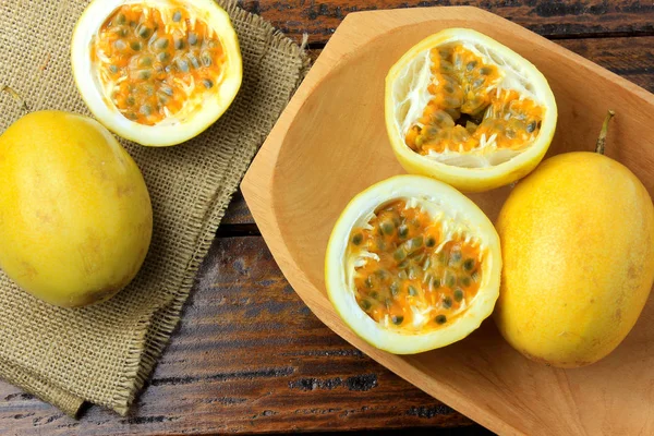 yellow passion fruit and passion fruit cut in half in wooden bowl on wooden table.Top view