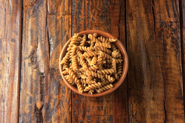 Top view Wholemeal Pasta. Integral fusilli into bowl over a wooden table. Copy space
