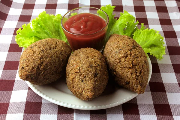 Kibbeh frito com molho de tomate em um prato, na mesa forrada com toalha de mesa quadriculada — Fotografia de Stock