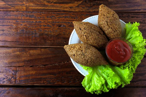 Kibbeh frito com molho de tomate em uma chapa, sobre mesa de madeira rústica — Fotografia de Stock