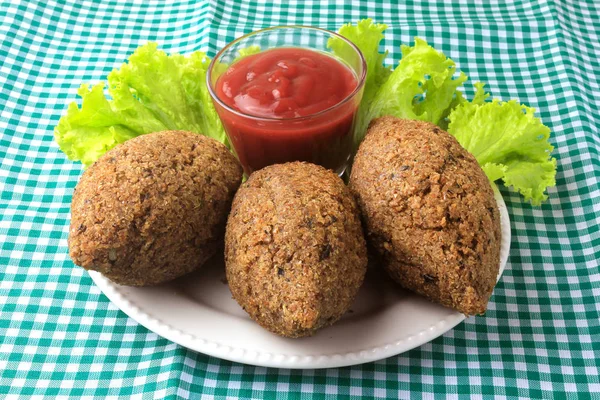 Kibbeh frito com molho de tomate em um prato, na mesa forrada com toalha de mesa quadriculada — Fotografia de Stock