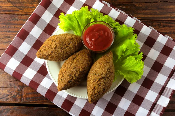 Kibbeh frito con salsa de tomate en un plato, sobre una mesa de madera rústica — Foto de Stock