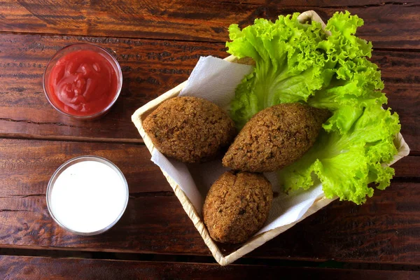 Gebratene Kibbeh mit Tomatensauce im Korb, über rustikalem Holztisch — Stockfoto