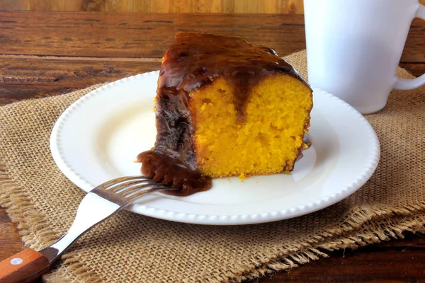 slice of carrot cake with chocolate coating on white ceramic plate on rustic wooden table