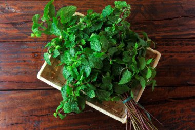 Rustik ahşap masa üzerinde sepet içinde yeşil organik taze nane grubu. Şifalı ve mutfak kullanımları ile aromatik nane