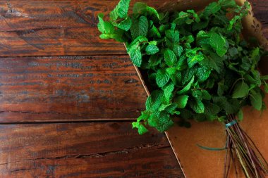 Rustik ahşap masa üzerinde sepet içinde yeşil organik taze nane grubu. Şifalı ve mutfak kullanımları ile aromatik nane