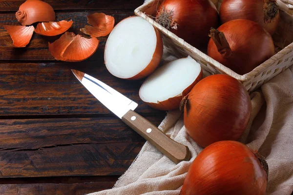 Verse en gesneden organische uien in mand en verspreid over rustieke houten tafel in de keuken — Stockfoto