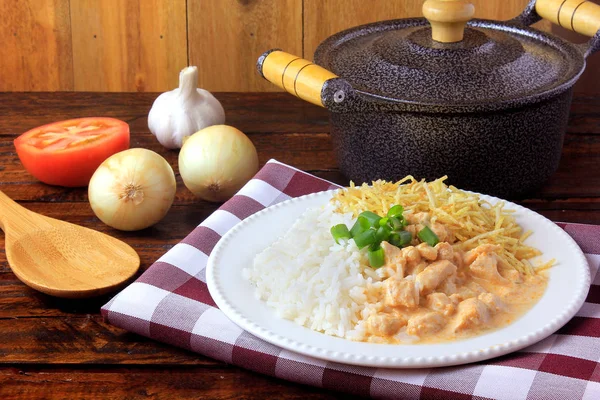 Ayam stroganoff, panci dan bahan-bahan. Di Brasil, hidangan tersebut terdiri dari krim asam dengan ekstrak tomat, nasi dan stik kentang, di atas meja kayu pedesaan . — Stok Foto