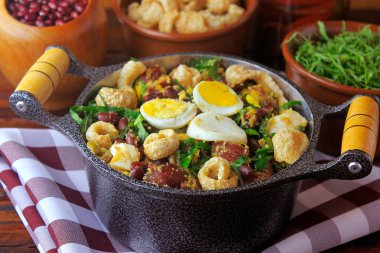 Fasulye, pastırma, sosis, collard yeşillik, yumurta, rustik ahşap masada yapılan Brezilya mutfağının Feijao Tropeiro tipik yemek,.
