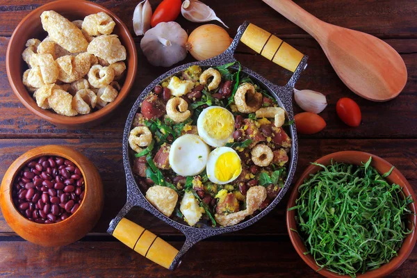 Feijao Tropeiro prato típico da culinária brasileira, feito com feijão, bacon, salsicha, couve-flor, ovos, em mesa de madeira rústica . — Fotografia de Stock