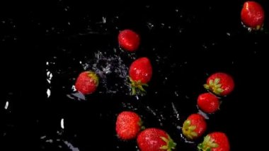 Taze çilek su siyah arka plan üzerine düşüyor. Sağlıklı beslenme kavramı. Taze meyve arka plan. Ağır çekim görüntüleri.