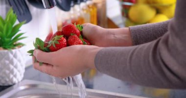Kadın elleri mutfakta çilek yıkıyor. Taze ve sağlıklı meyve konsepti yemek. Yakın çekim 4k