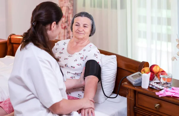 Kadın doktor evde ya da bakımevinde kan basıncını ölçüyor. Yaşlılar için sağlık hizmeti kavramı.