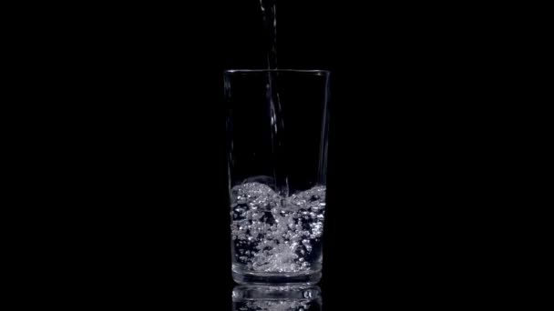 Remplissage d'un verre d'eau minérale fraîche sur fond noir. Boire sainement. Images au ralenti à 180 ips.