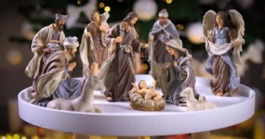 Noel ağacının önündeki beyaz masada atmosferik ışıklarla İsa Mesih 'in İsa' nın doğumu sahnesi. Heykellerle Noel sahnesi. Dolly 4K çekti.
