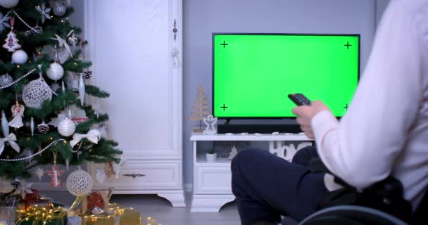 クリスマスにテレビの緑の画面を見て遠隔操作で車椅子の男 ドリーショット4K — ストック動画
