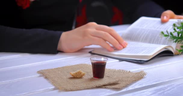 年轻的女人读圣经 带着圣经上的圣餐 耶稣基督的血和身体的酒和面包符号 专注于玻璃 Closeup Dolly Shot — 图库视频影像