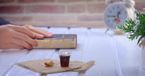 聖書を読んで聖餐式を取る若い女性 聖書とイエス キリストの血と体のワインとパンのシンボル ガラスに集中しろ クローズアップドリーショット4K — ストック動画